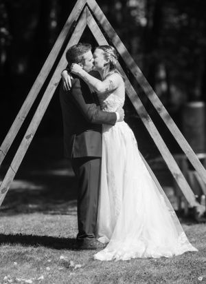 Black and white wedding kiss under triangular wooden arch.