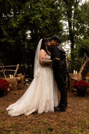 Wedding couple embracing outdoors with rustic fall decor and woodpile.
