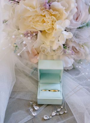 Delicate wedding details including white flowers and a mint green ring box on lace fabric.