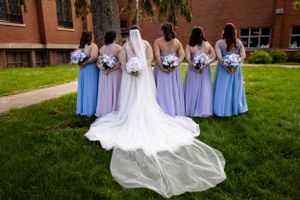 Wedding party in light blue dresses standing on green lawn with church building in background.