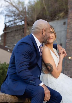 Wedding couple shares an intimate moment outdoors against a rustic brick wall backdrop.