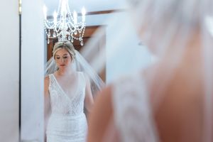 Romantic bridal portrait reflected in mirror with chandelier and flowing veil.