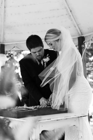 Black and white photo of couple signing documents during outdoor ceremony under tent.