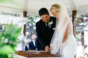 Couple signs wedding documents under white tent during outdoor ceremony.
