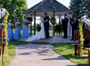 Wedding ceremony takes place under white gazebo with purple-clad attendants and floral decorations.