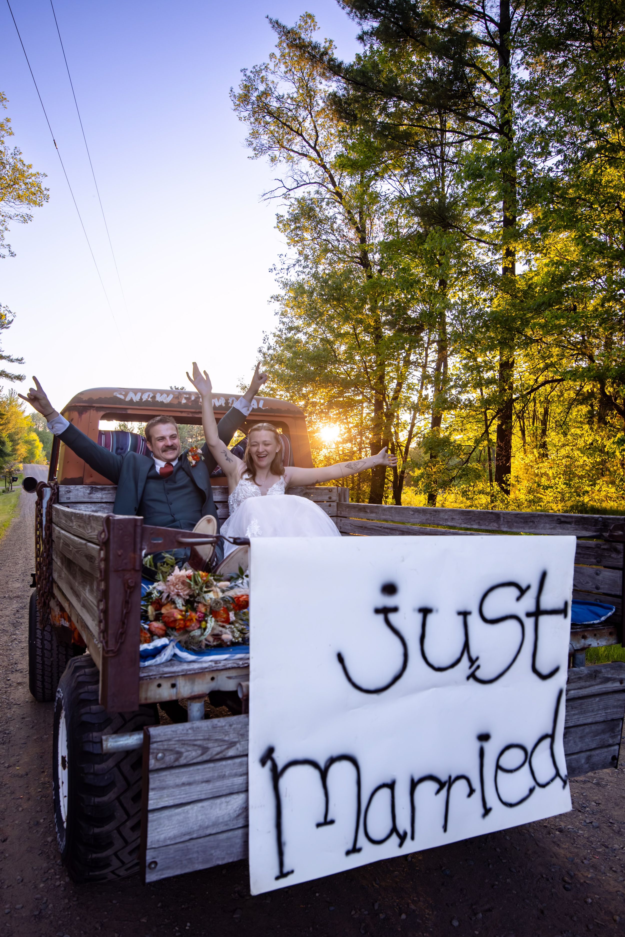 Newlyweds celebrate in vintage truck with Just Married sign at sunset.