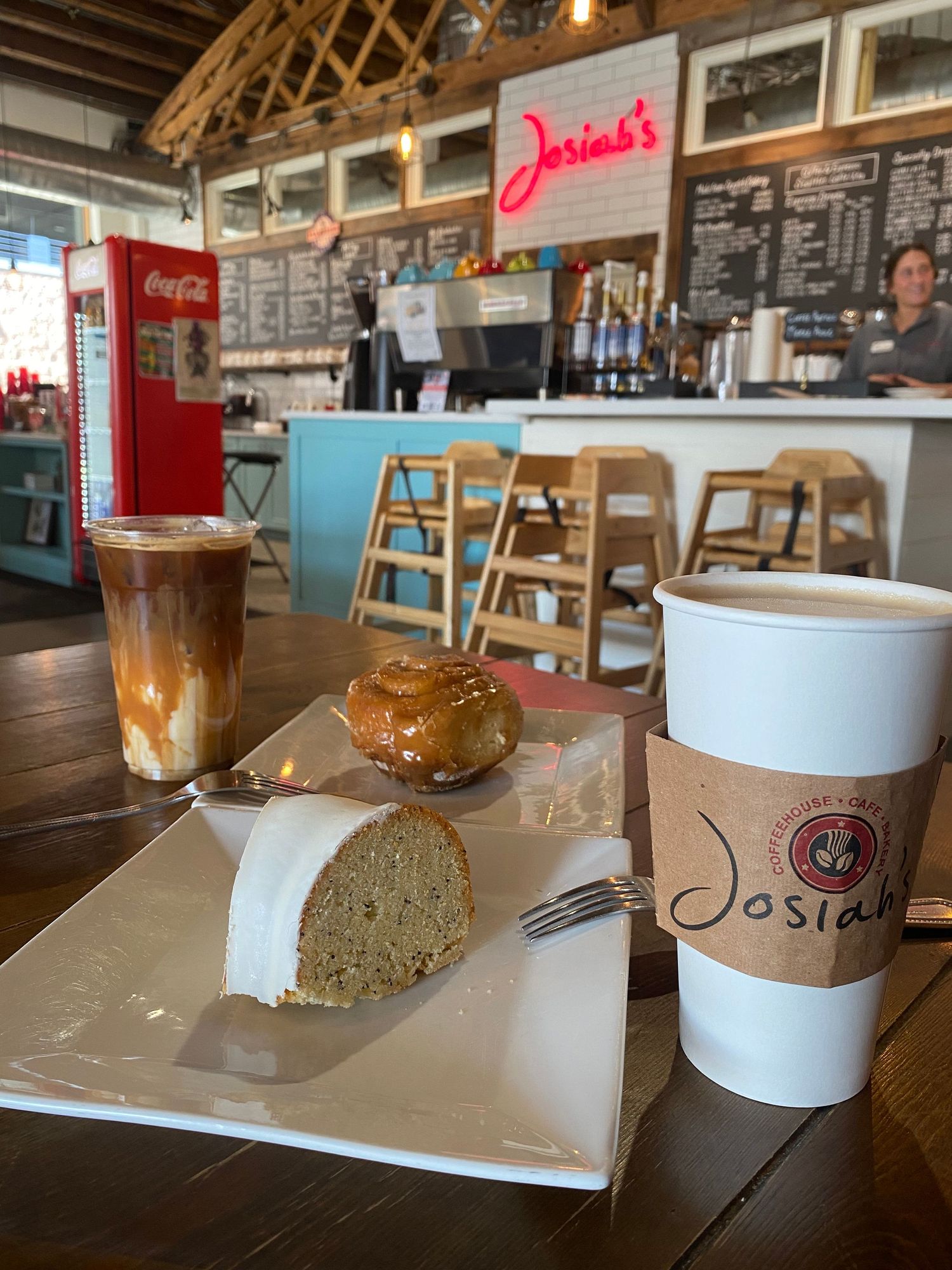Coffee shop interior with pastries and beverages on a wooden table near a counter with menu boards.