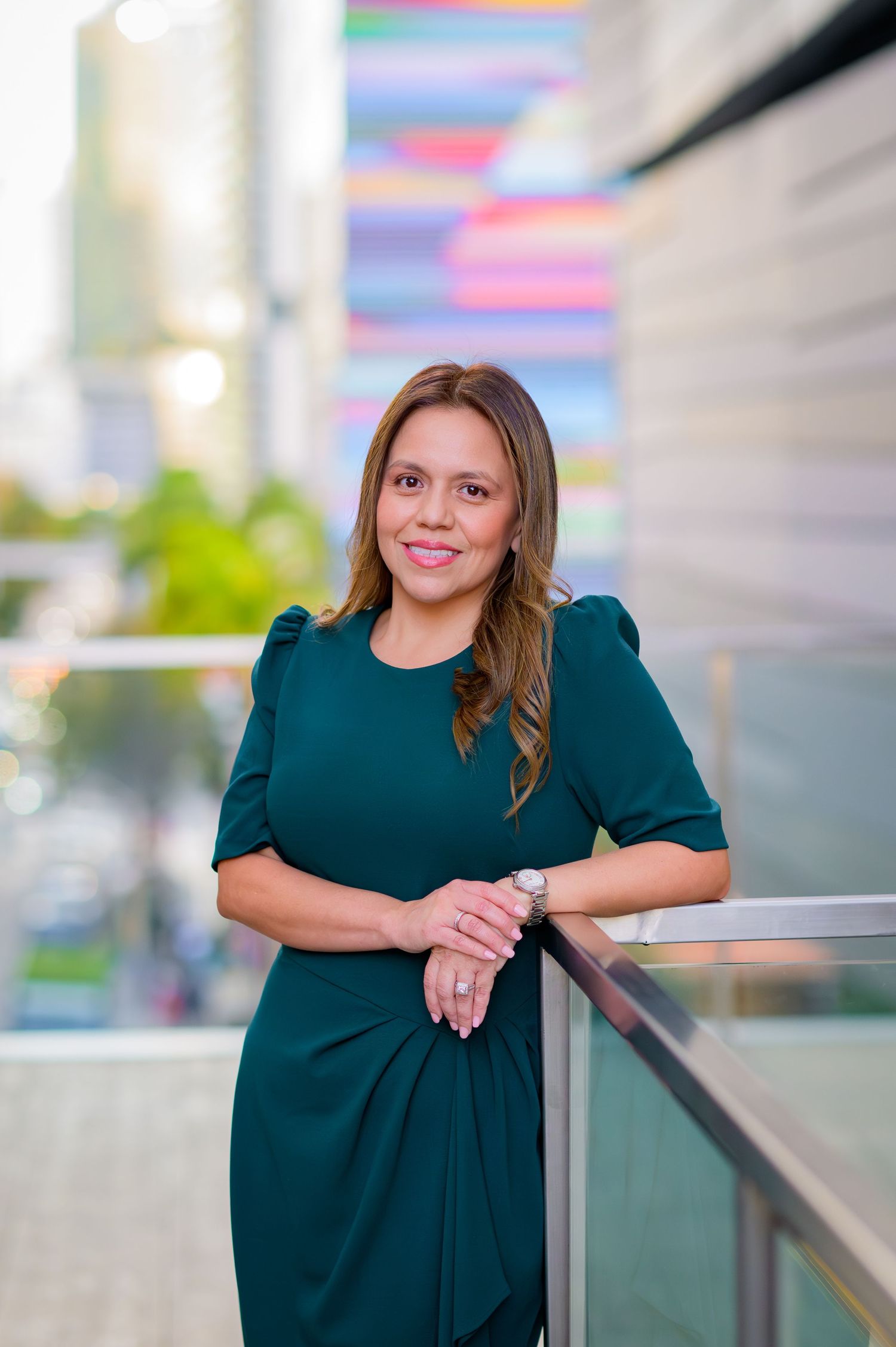 Woman in emerald green dress poses confidently against urban backdrop with colorful elements.