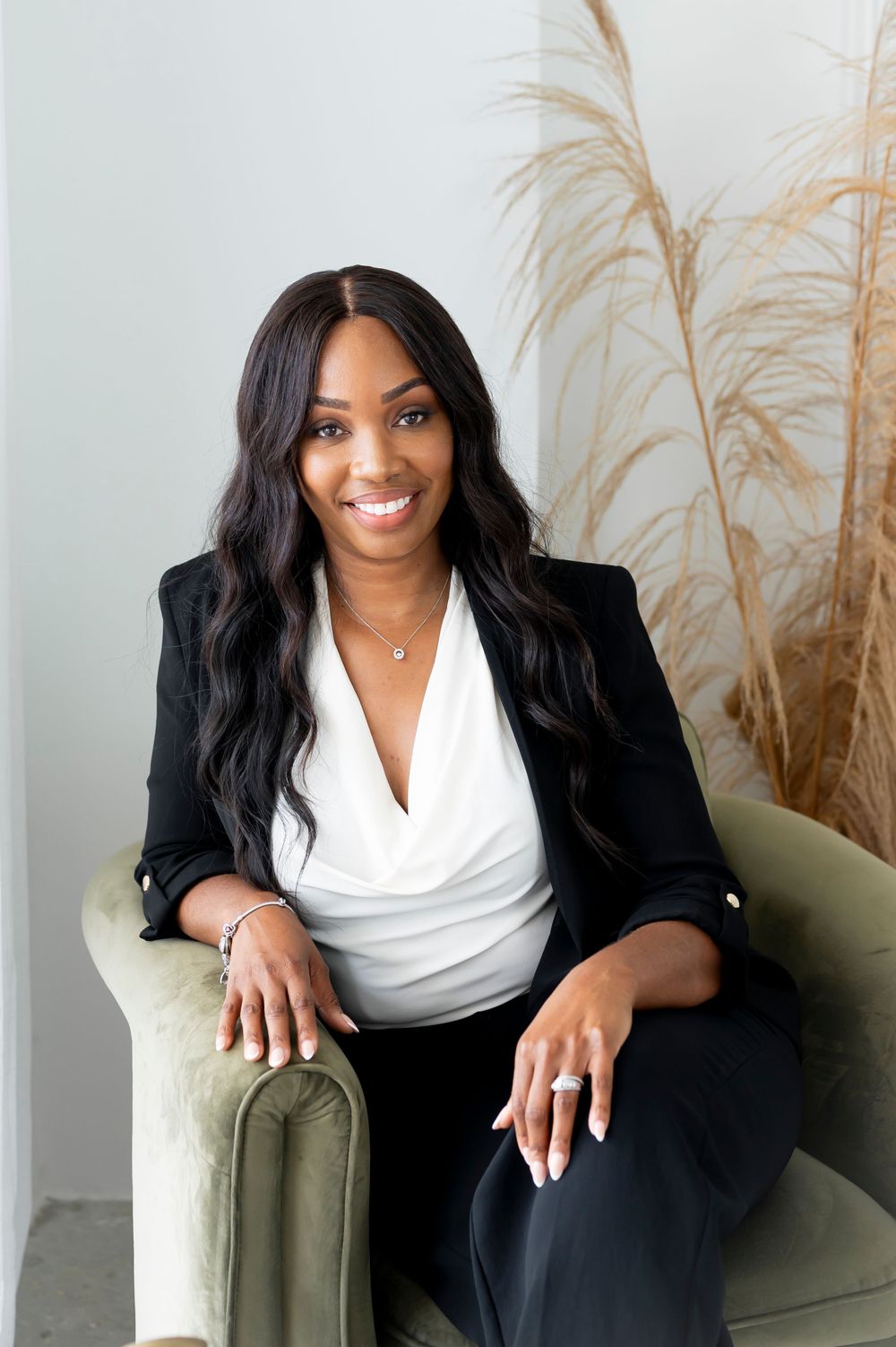 Professional portrait of woman in black blazer and white top seated on green chair.