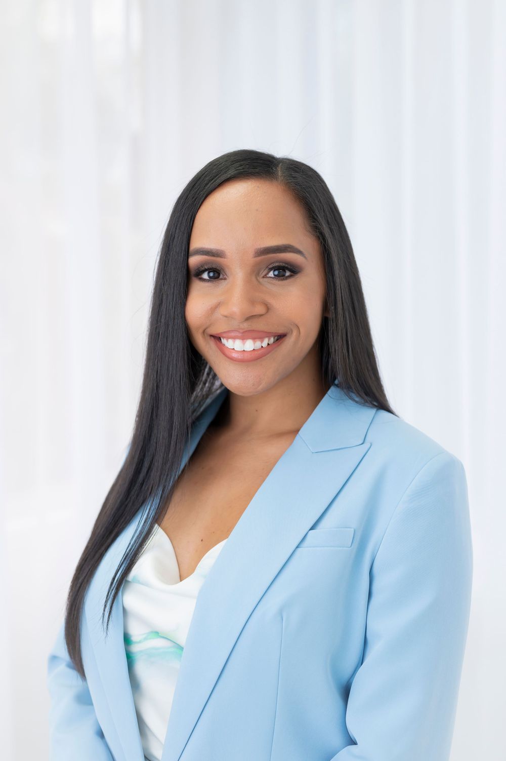 Professional portrait of woman wearing light blue blazer against white background.