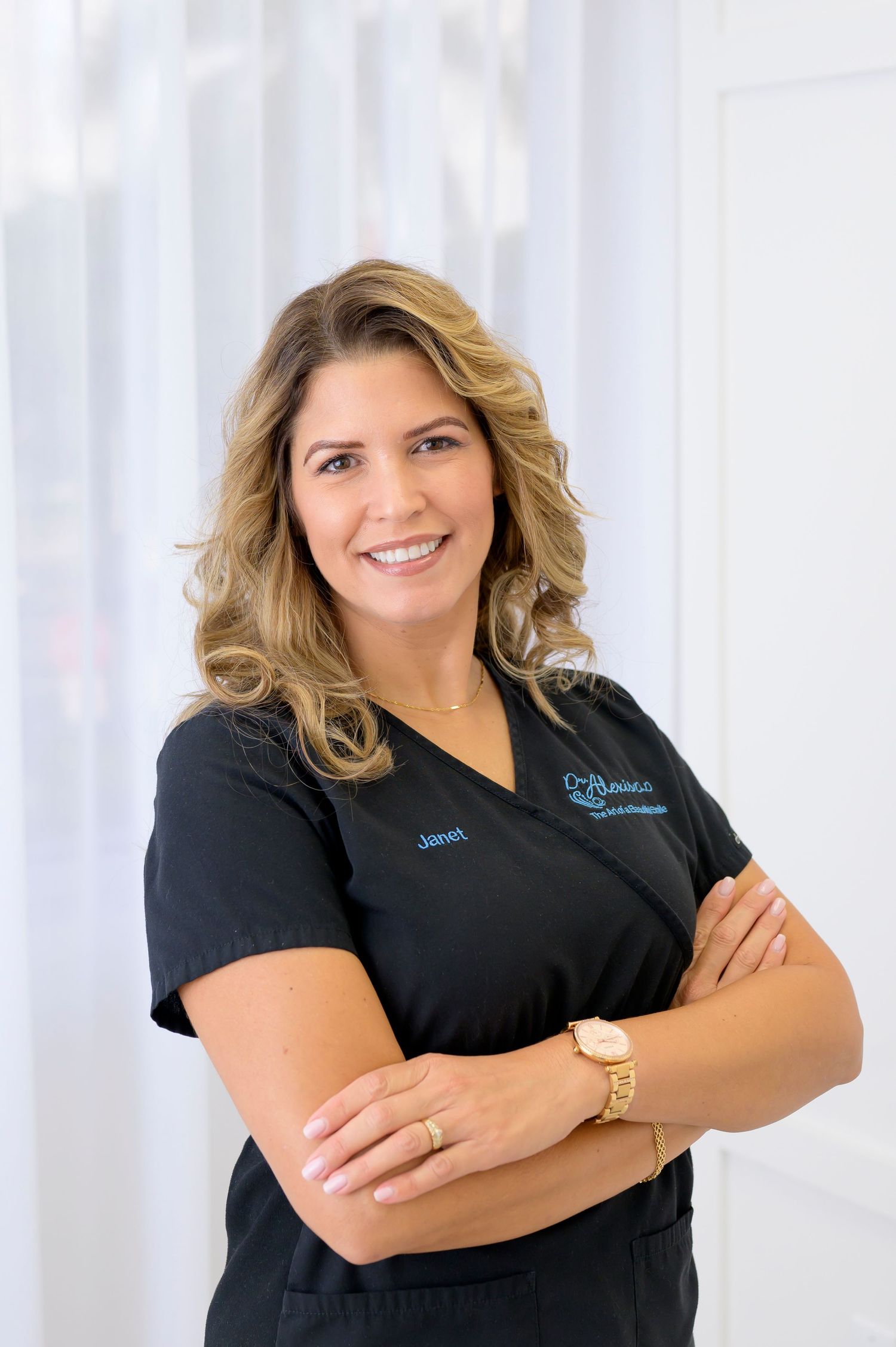 Healthcare worker in dark scrubs poses confidently with arms crossed in medical office setting.