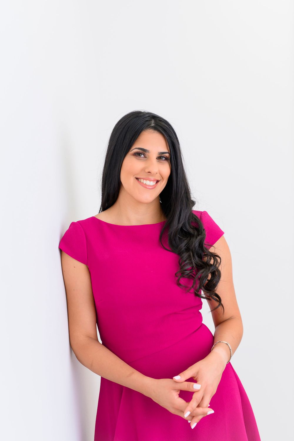Woman in bright pink dress poses against white background in professional portrait setting.