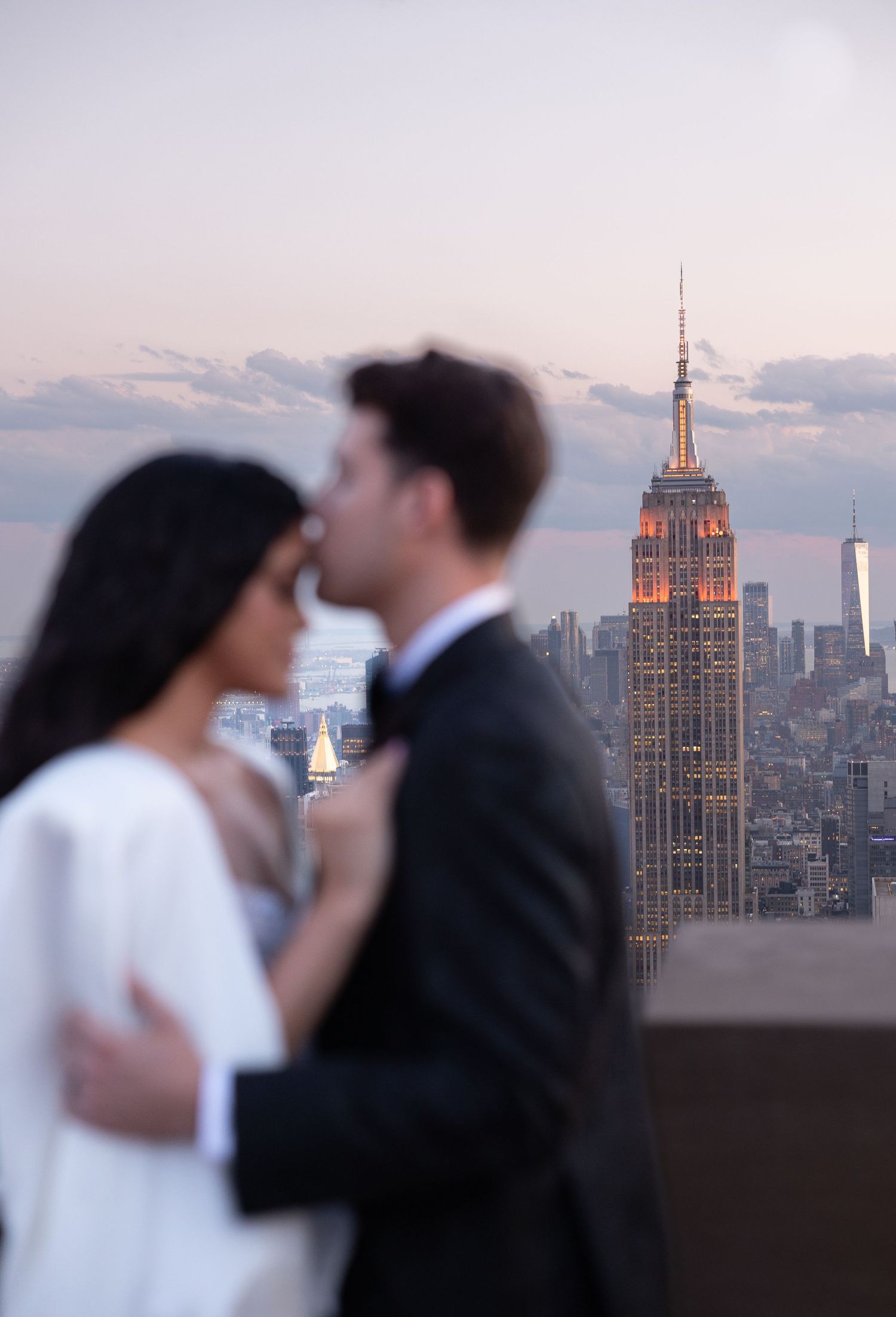 Wedding couple embracing with Empire State Building visible in background during sunset.