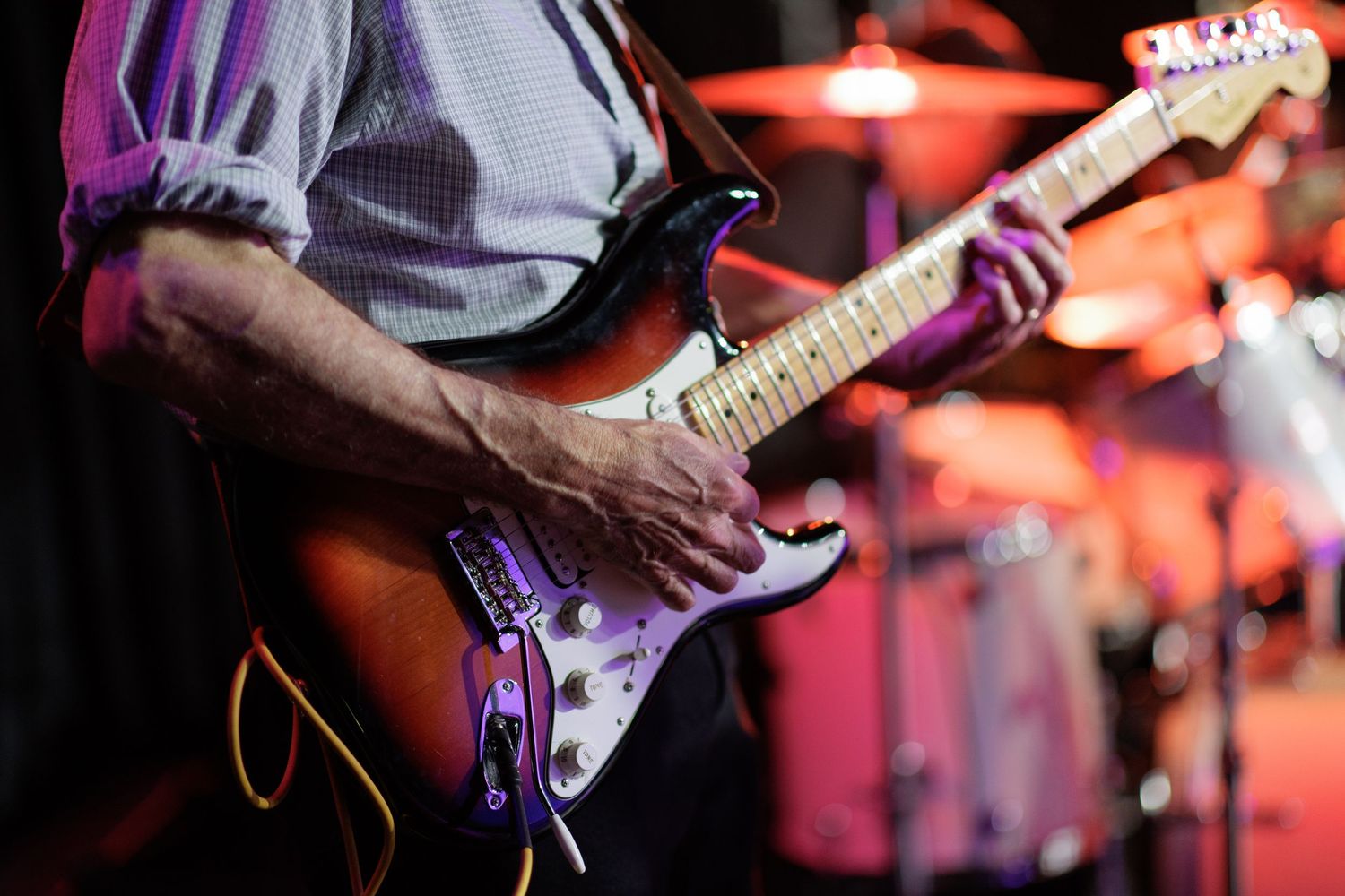 A musician performs on stage with an acoustic guitar under dramatic concert lighting.
