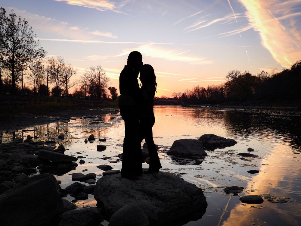 Couple embrace on a rock in a river at sunset in Logansport.