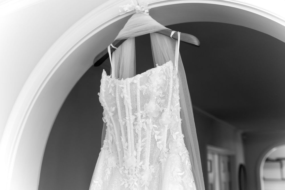 Close-up details of delicate lace wedding dress hanging against white background.