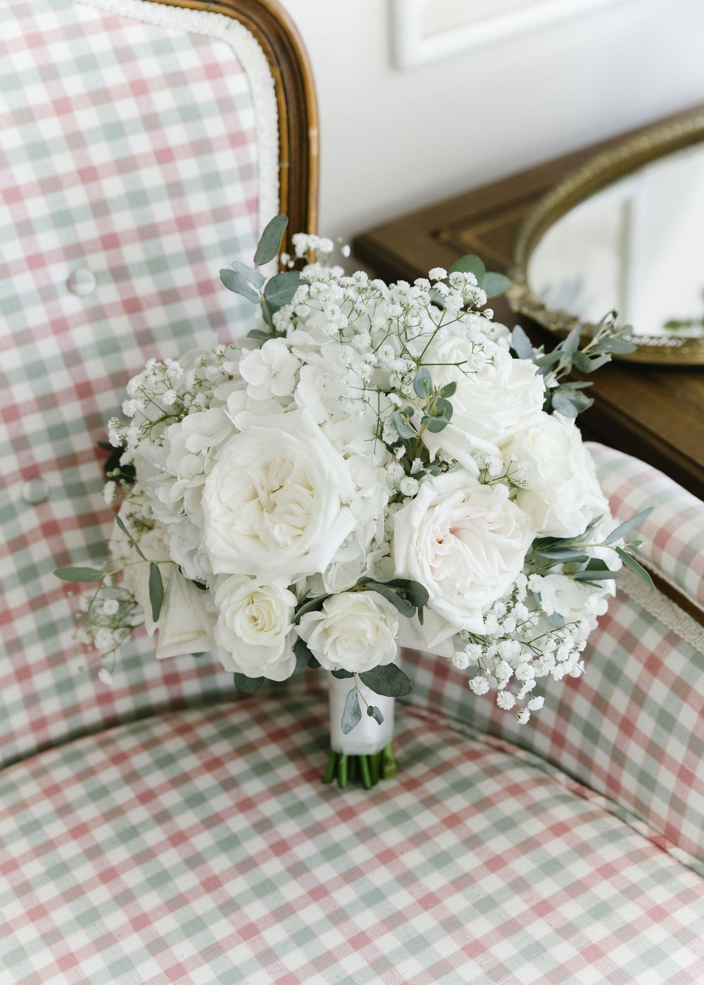 White roses and baby's breath bouquet arranged on pink and white gingham fabric.