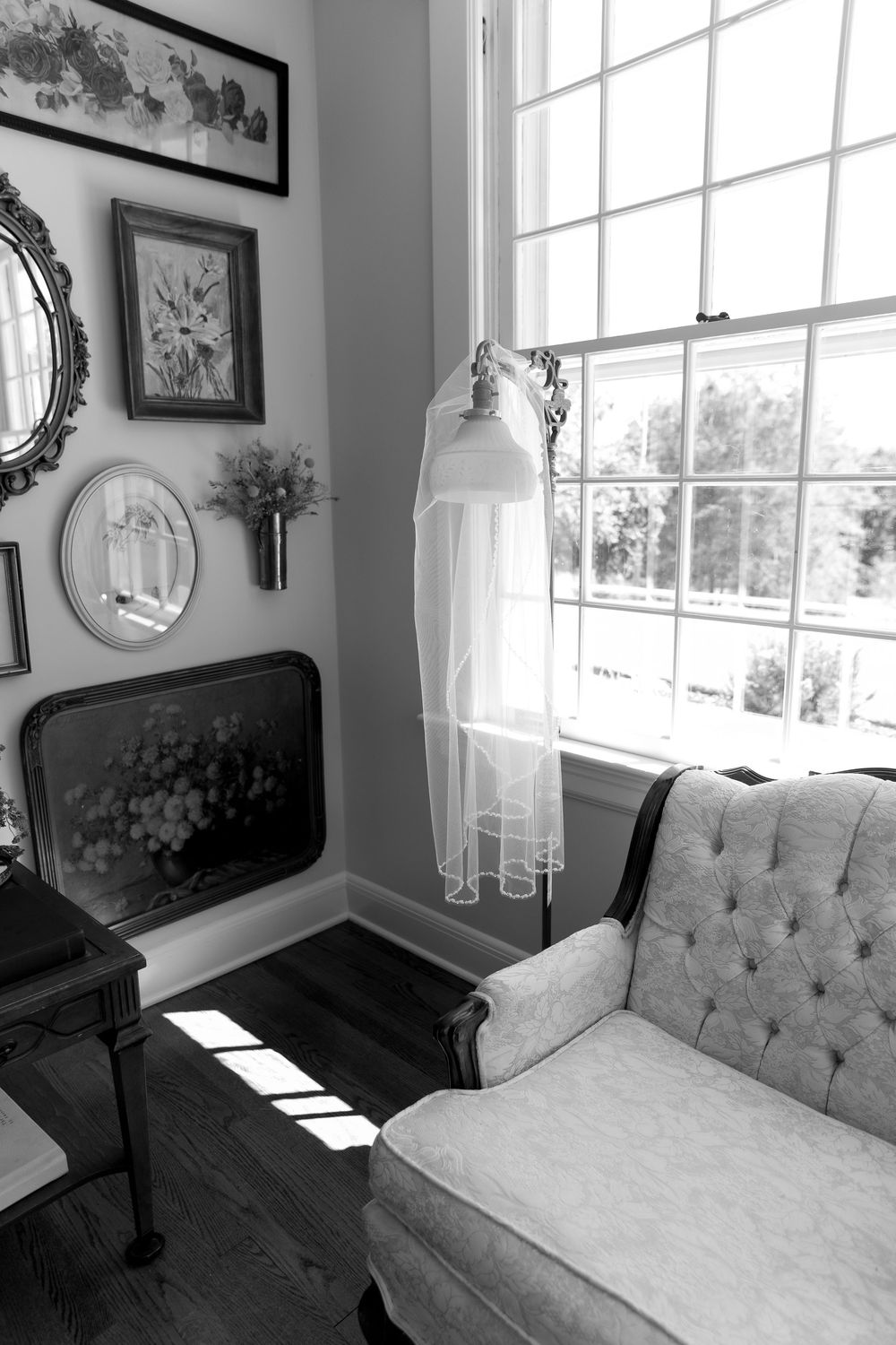 A bright and airy bedroom with tufted gray seating near large windows and framed artwork on the walls.