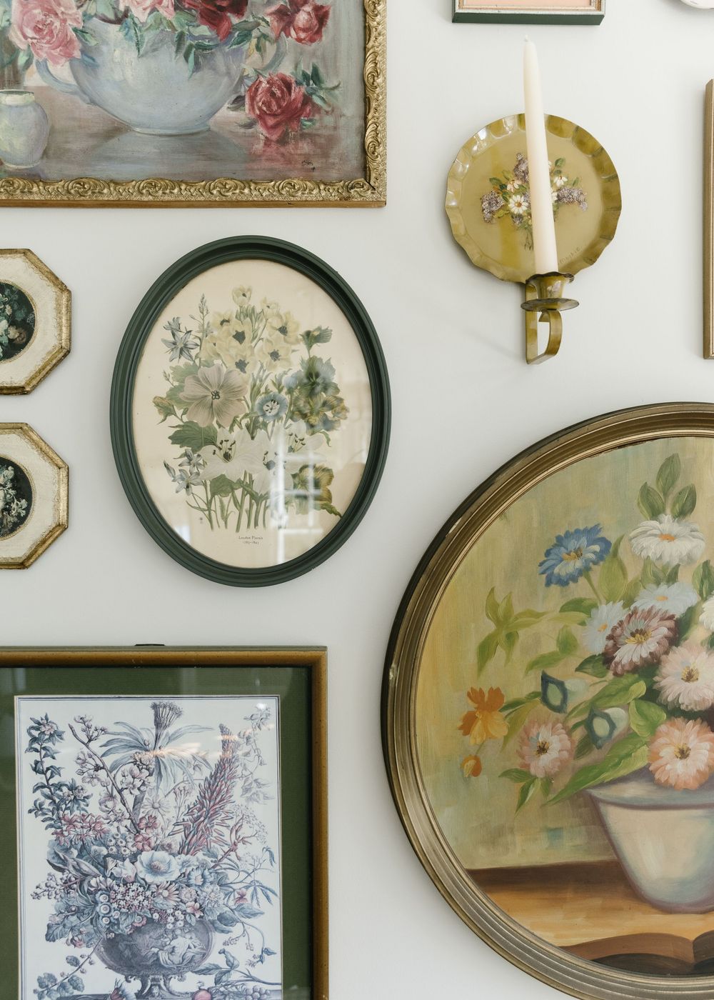 A collection of vintage floral artwork and framed botanical prints arranged on a white wall.