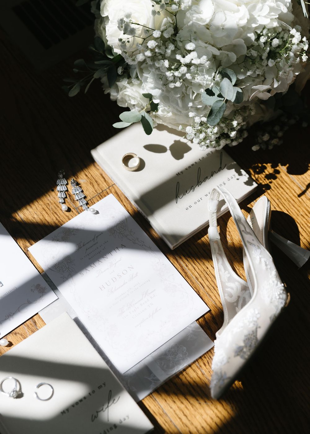 Wedding rings casting shadows on a wooden surface with white floral decorations.