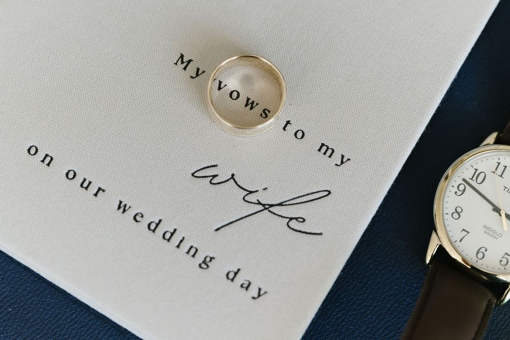 A close-up view of elegant wedding invitation text printed on white paper with a gold ring in the background.
