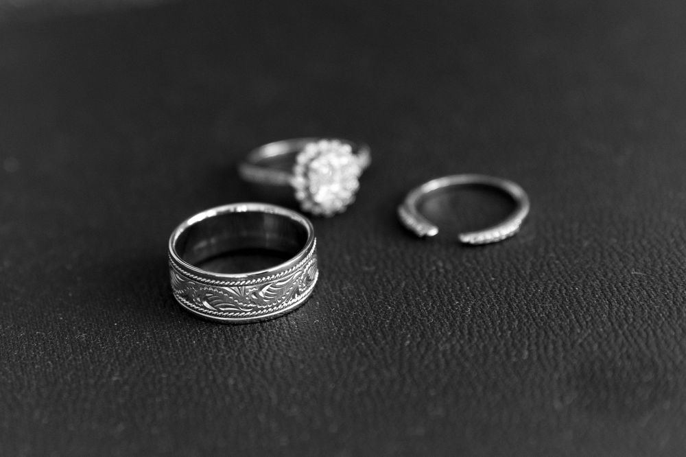Black and white photo of three wedding rings including an engagement ring and bands on dark leather surface.