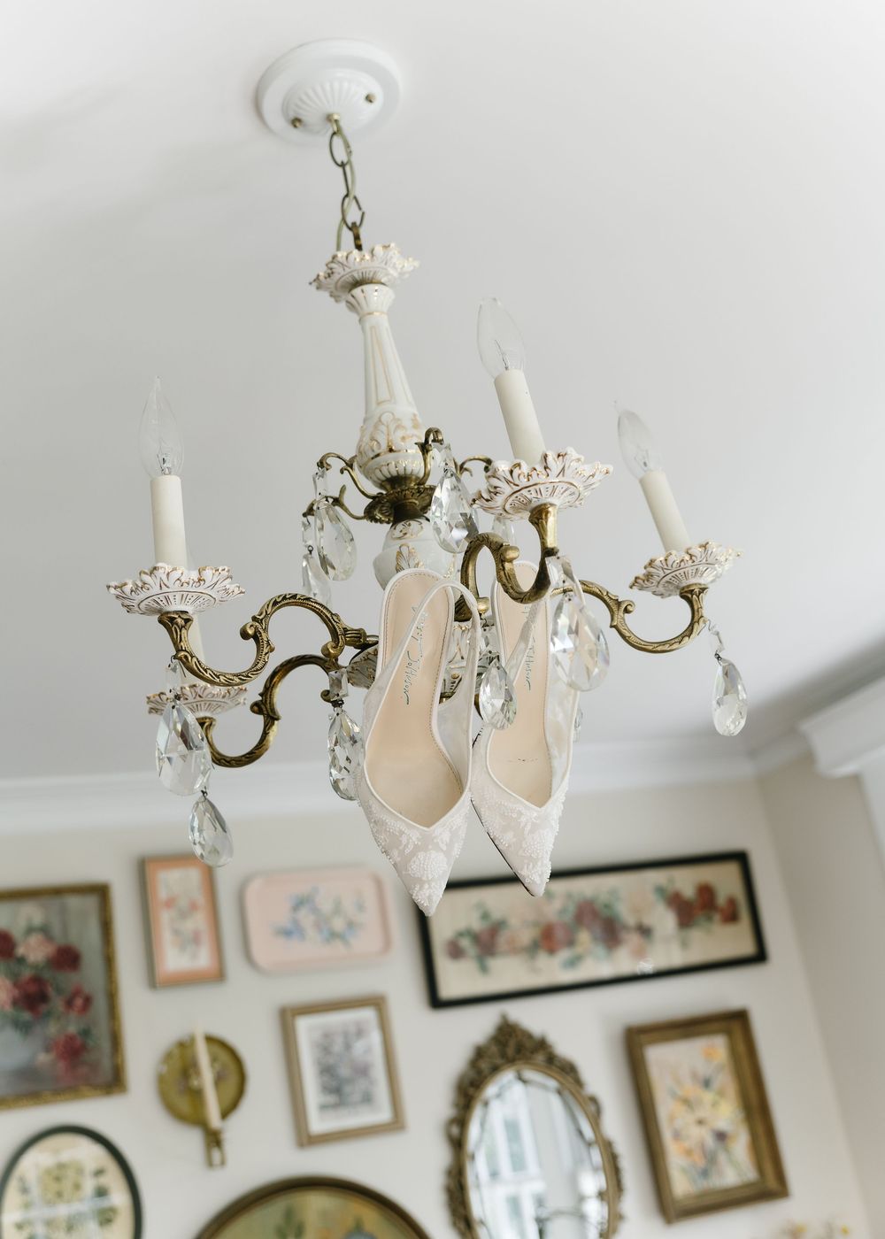 Elegant crystal chandelier with white bridal shoes hanging from it in a vintage-style room.