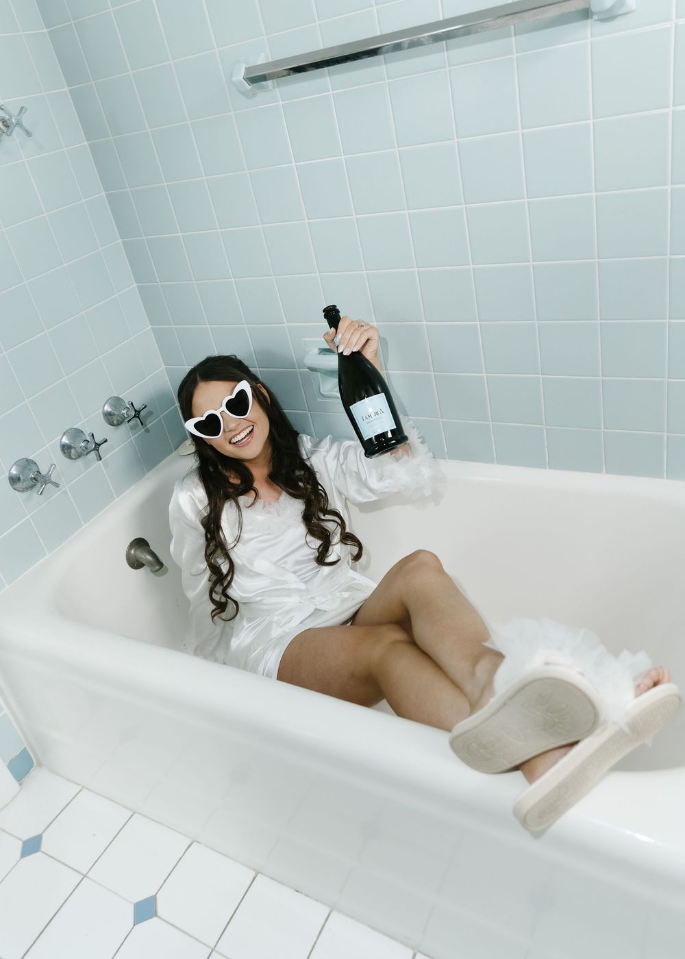 Person relaxing in a white bathtub wearing sunglasses and white clothing.