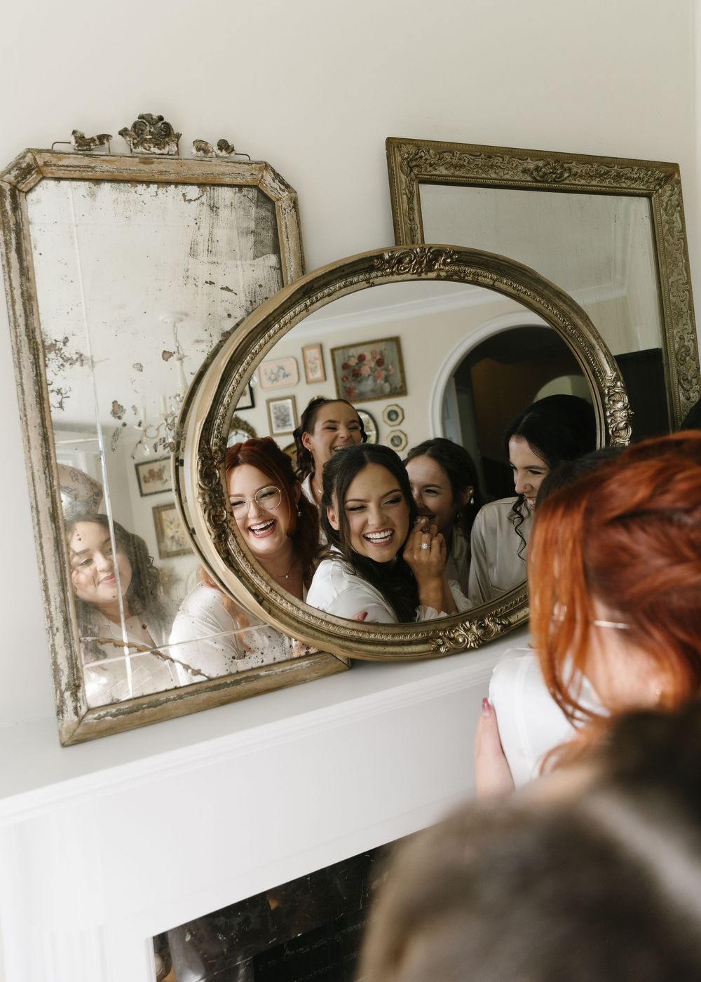 A group of people reflected in vintage ornate mirrors mounted on a wall, showing joyful expressions.