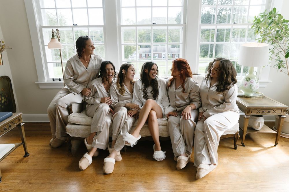 Wedding party relaxes together in white robes by sunlit windows during pre-ceremony preparations.