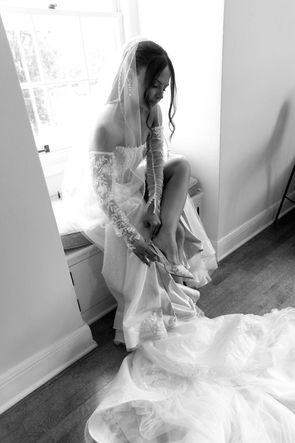 A flowing white wedding dress with delicate lace details captured in natural window light.