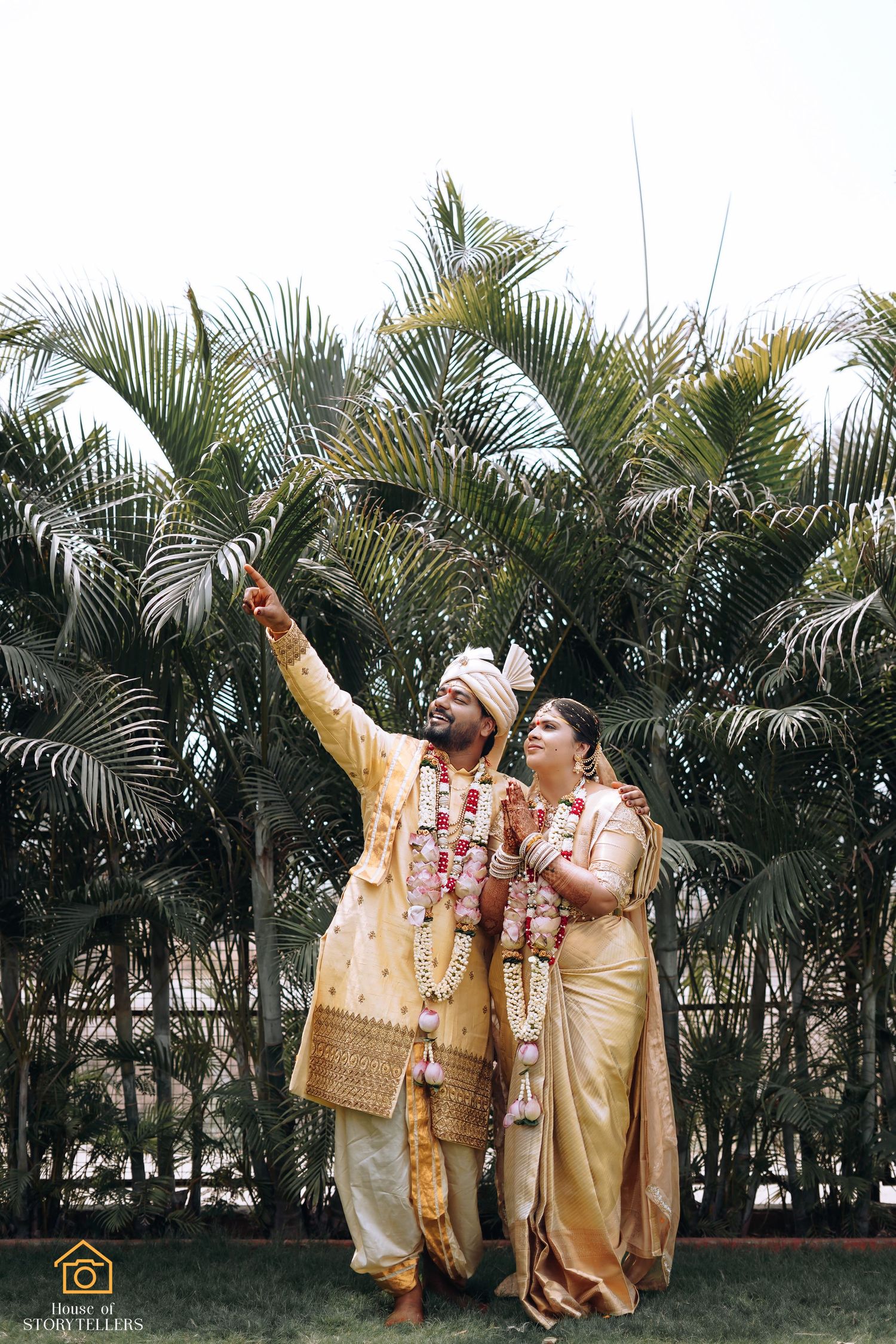 Joyful couple in traditional wedding attire posing against palm trees.