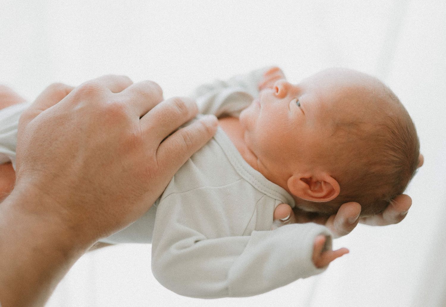 Gentle hands holding newborn baby against white background.