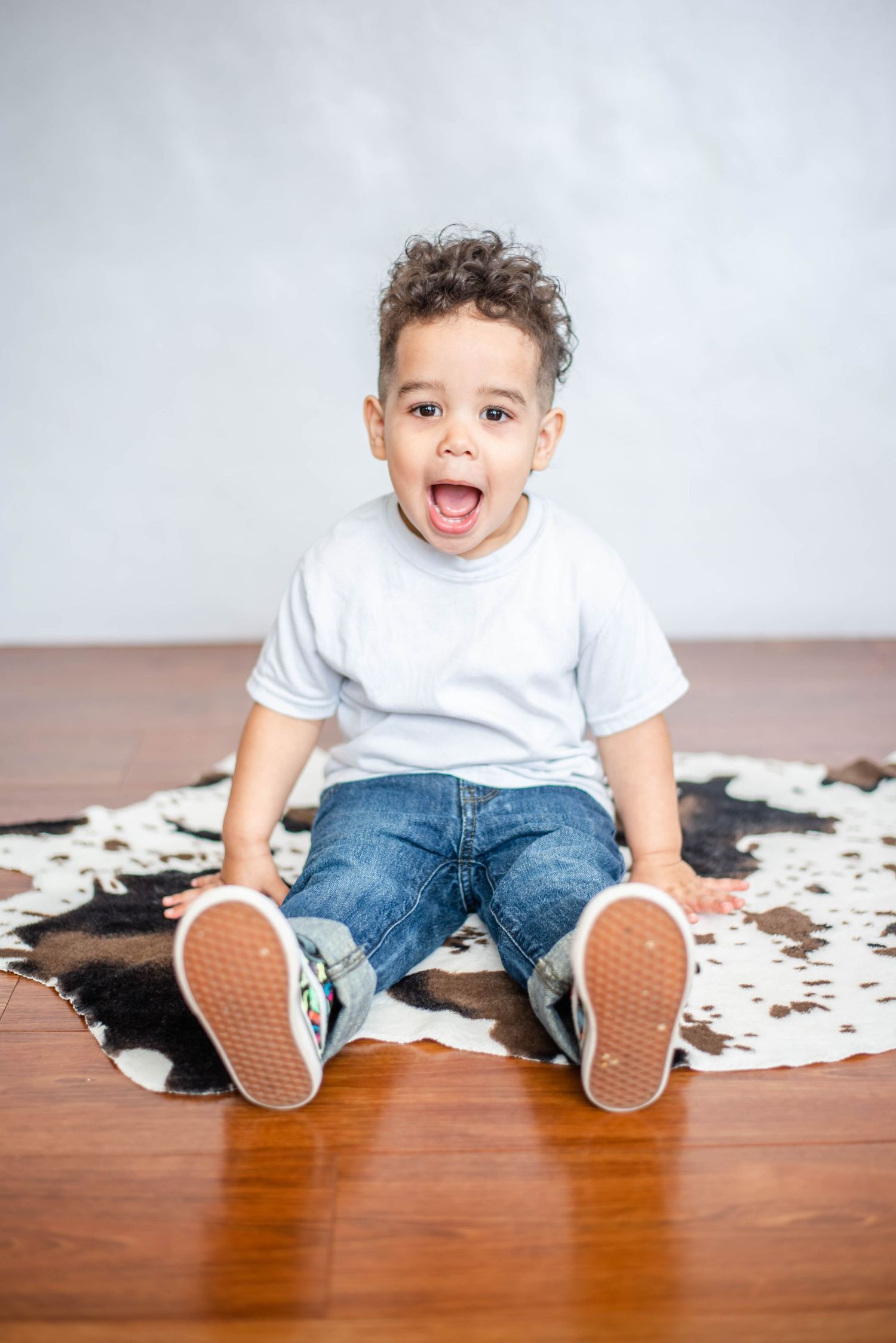 Excited child sitting on floor with legs stretched out on cowhide rug.