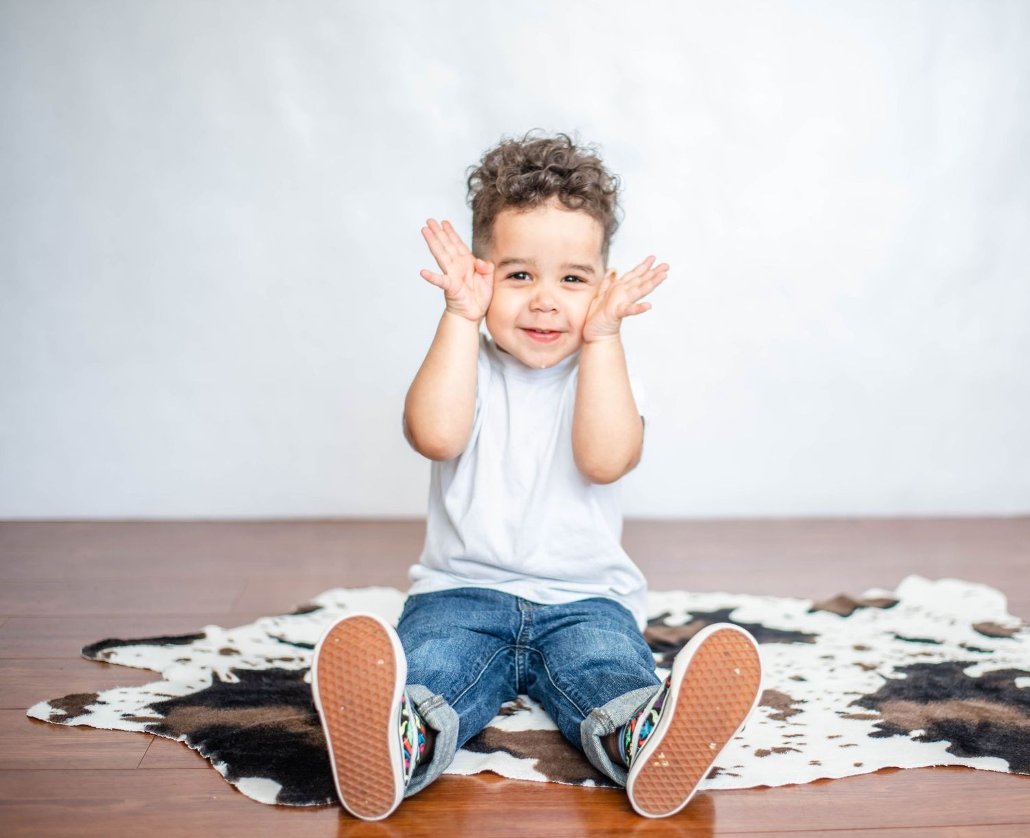 Child sitting on cowhide rug making playful face with hands near cheeks.