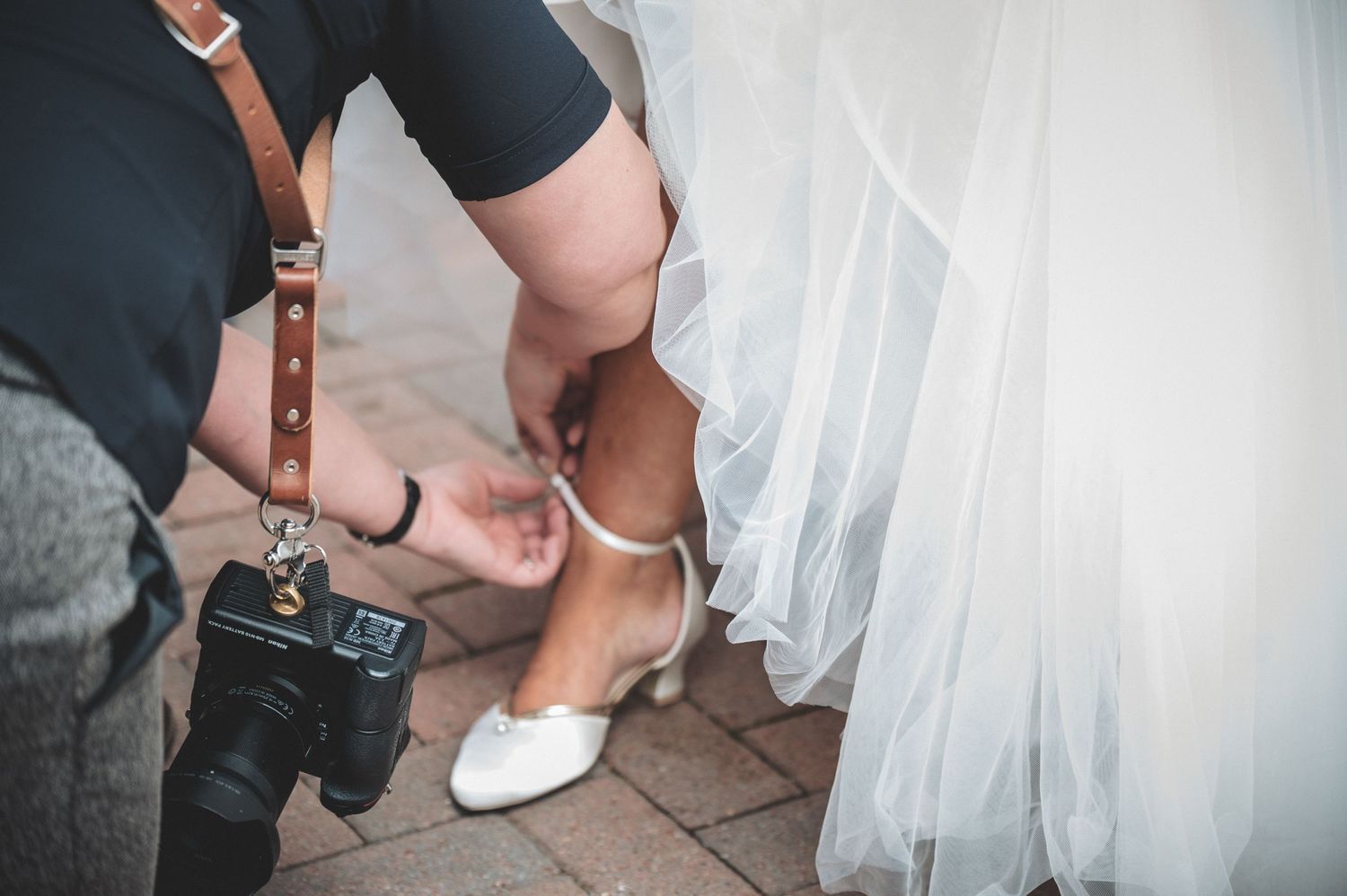 Wedding photographer crouches down to capture detail shot of bridal shoes.