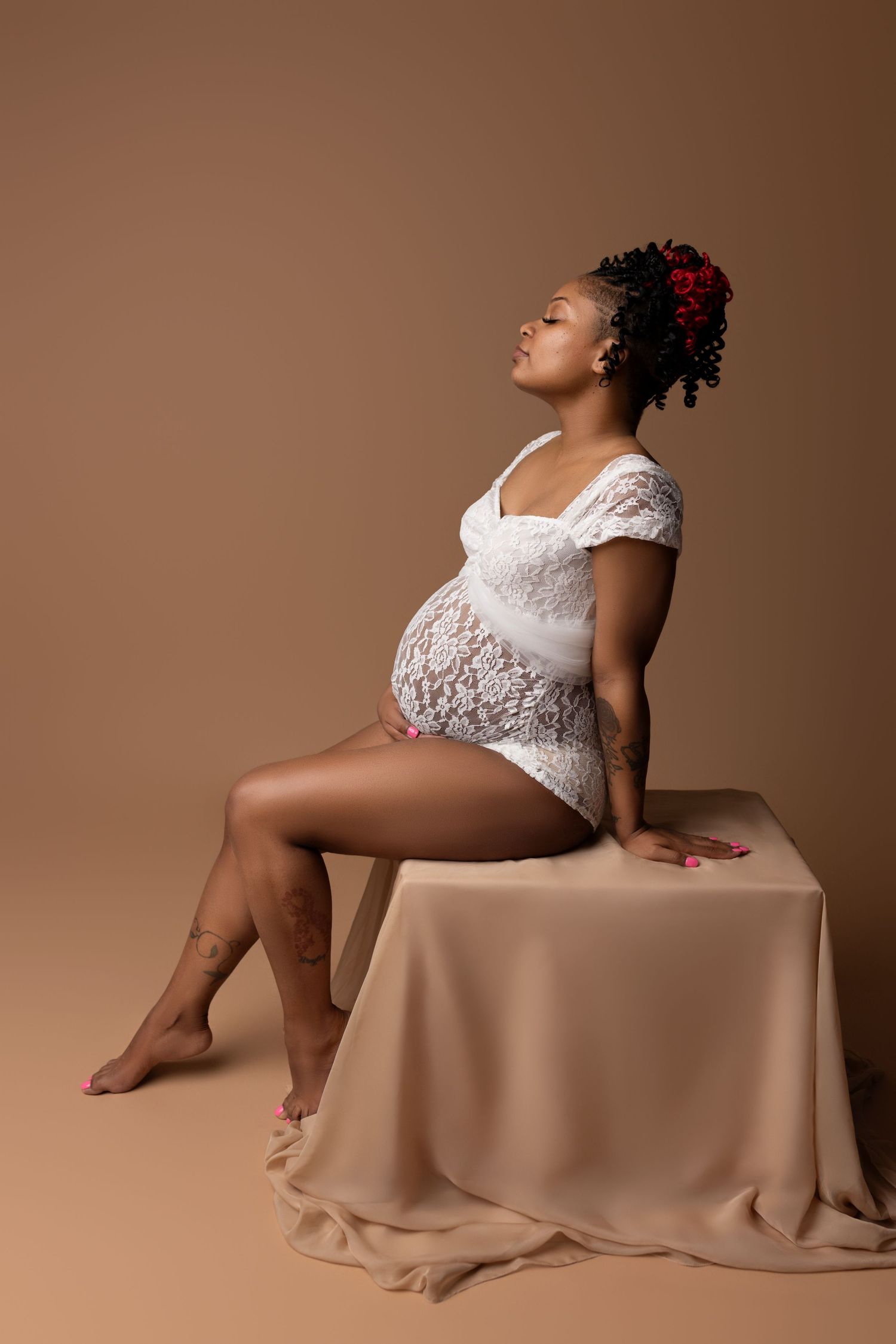 A glowing radiant mom-to-be, poses on a photo block, cupping her belly as she closes her eyes , dreaming of her baby.