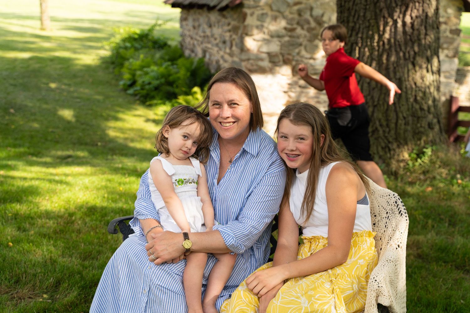 A relaxed family portrait taken outdoors on a sunny day with a stone building and trees in the background.