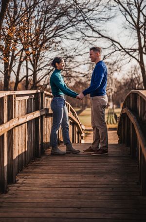 A couple stands together on a wooden bridge at sunset sharing an intimate moment in a park setting.