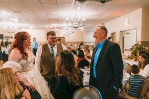 Bride in white gown and groom in suit chat with guests at elegant wedding reception venue.