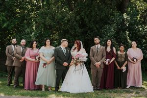 Wedding party poses outdoors in mismatched pink and taupe attire with bride and groom at center.