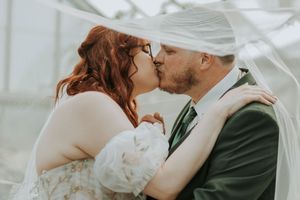 A bride and groom share a romantic kiss under a flowing veil during their wedding ceremony.
