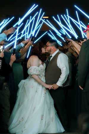 Bride and groom kissing under crossed blue lightsabers held by guests at a Star Wars themed wedding.