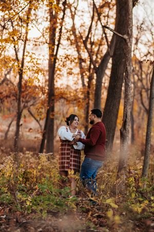 A romantic couple shares tender moments in a wooded area during fall, surrounded by golden sunlight and trees.