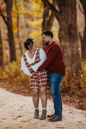 A couple in autumn attire shares a tender moment on a leaf-covered path surrounded by golden fall foliage.