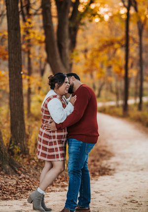 A couple shares intimate moments on a tree-lined autumn path with golden foliage and fallen leaves.