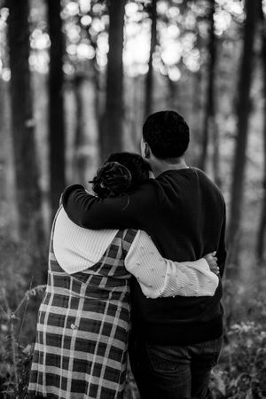 A couple embraces in a romantic black and white photo series set against a blurred forest background.