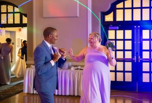 Two wedding guests share a dance together at a reception venue with blue lighting and elegant decor.