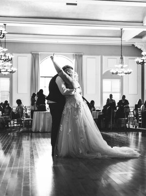 A panoramic black and white view of a dance studio with elegant wedding dresses displayed along the perimeter.
