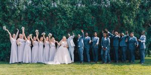 Wedding party in formal attire poses together on green lawn for outdoor group photo.
